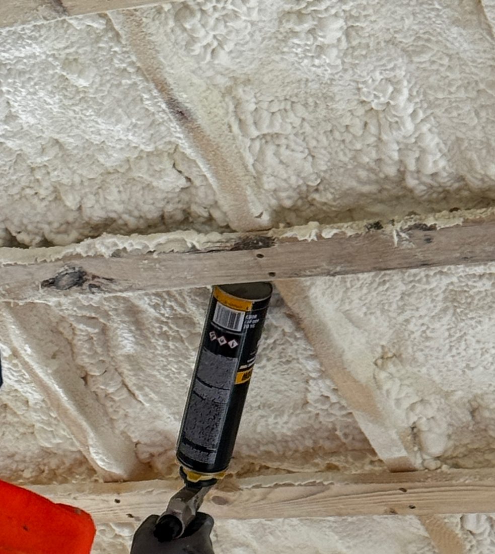 Spray foam insulation sprayed between roof rafters with a foam gun sealing gaps