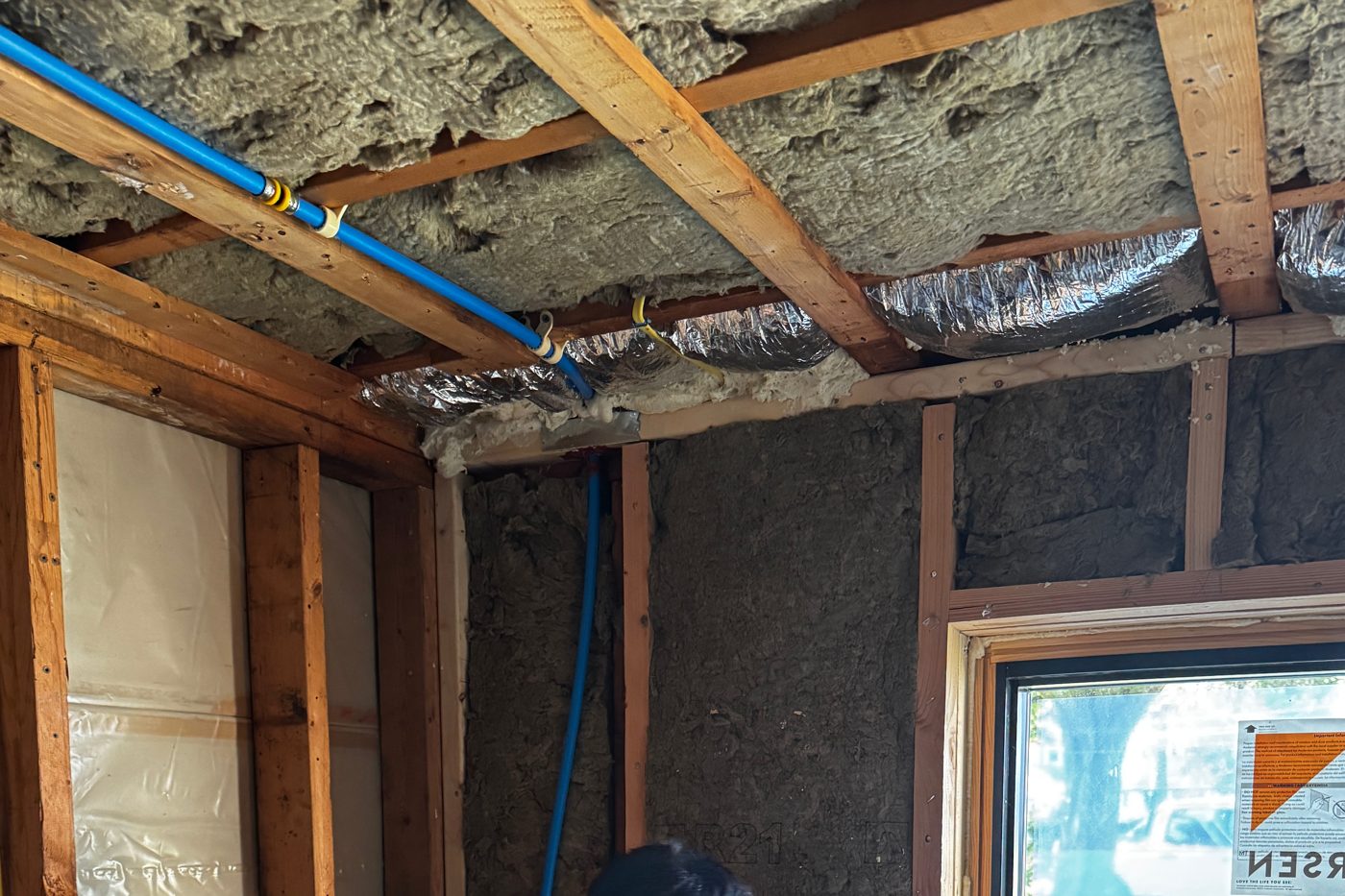 Wall cavities filled with insulation and a foil-faced ceiling during an insulation job near a new window